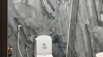 A bathroom with a toilet, shower, and sink against marble walls.