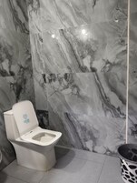 Baño con inodoro, paredes de mármol y un cubo de basura.