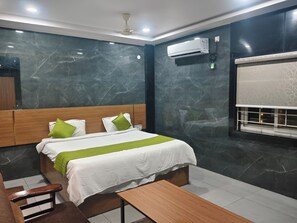 A modern hotel room with a marble wall, a bed with a green and white bedspread, a wooden headboard, a bedside table, and an air conditioning unit. - HoTEL MADHAVI PRIME  (Guntur)