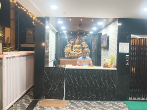 A hotel reception area with a receptionist, a Buddha statue, and a sign indicating the hotel's name and floors. - HoTEL MADHAVI PRIME  (Guntur)