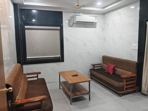 Una habitación pequeña y bien iluminada con un sofá, una mesa de madera y una ventana con un celosía decorativa.