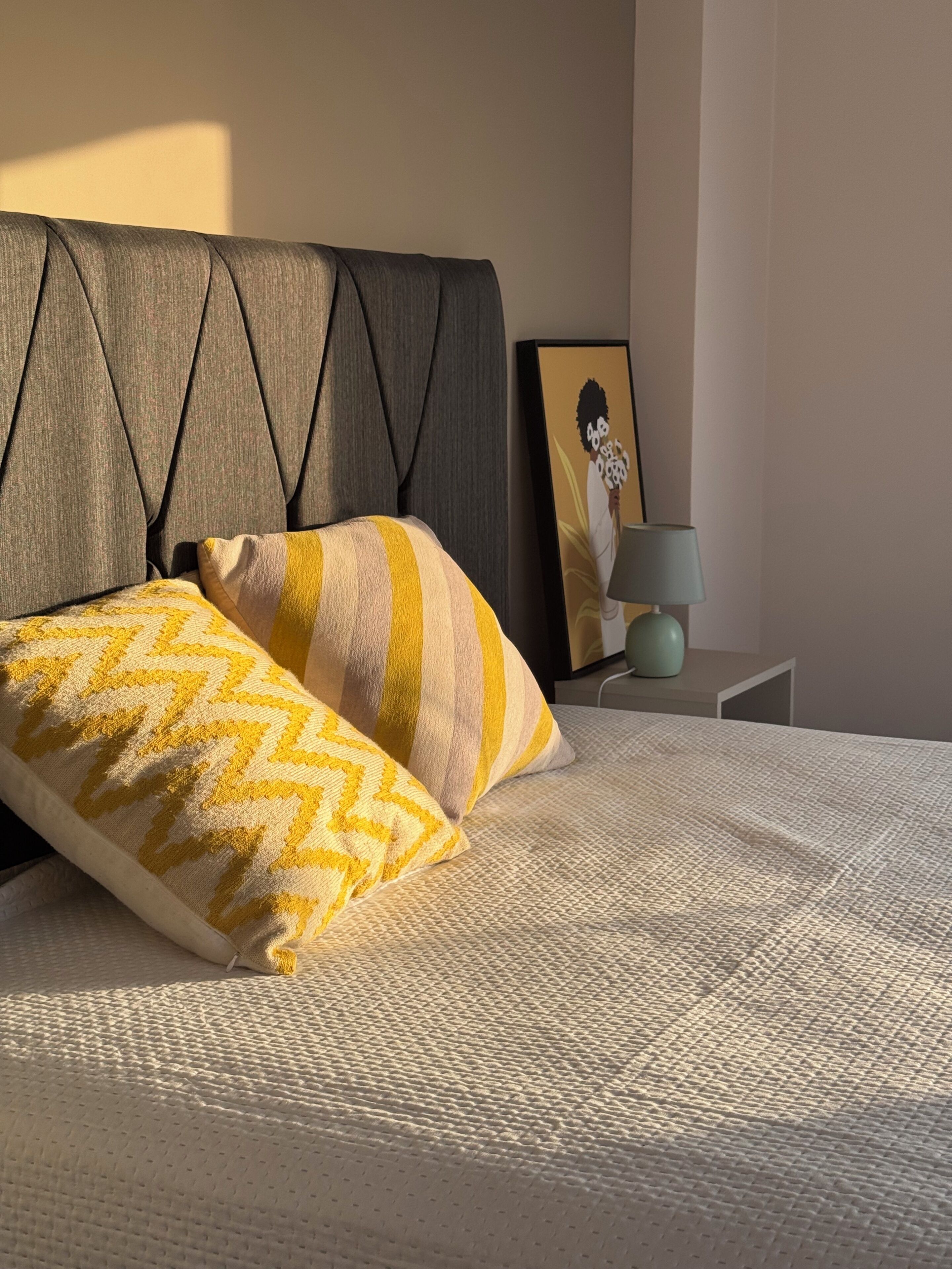 A bed with a textured white cover, a pillow with a chevron pattern, and a grey upholstered headboard.