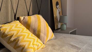A bed with a textured white cover, a pillow with a chevron pattern, and a grey upholstered headboard.