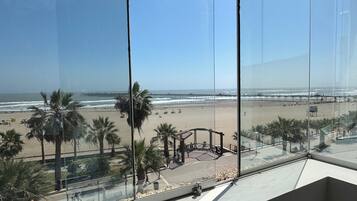 A view from a window overlooking a beach with palm trees and a boardwalk.