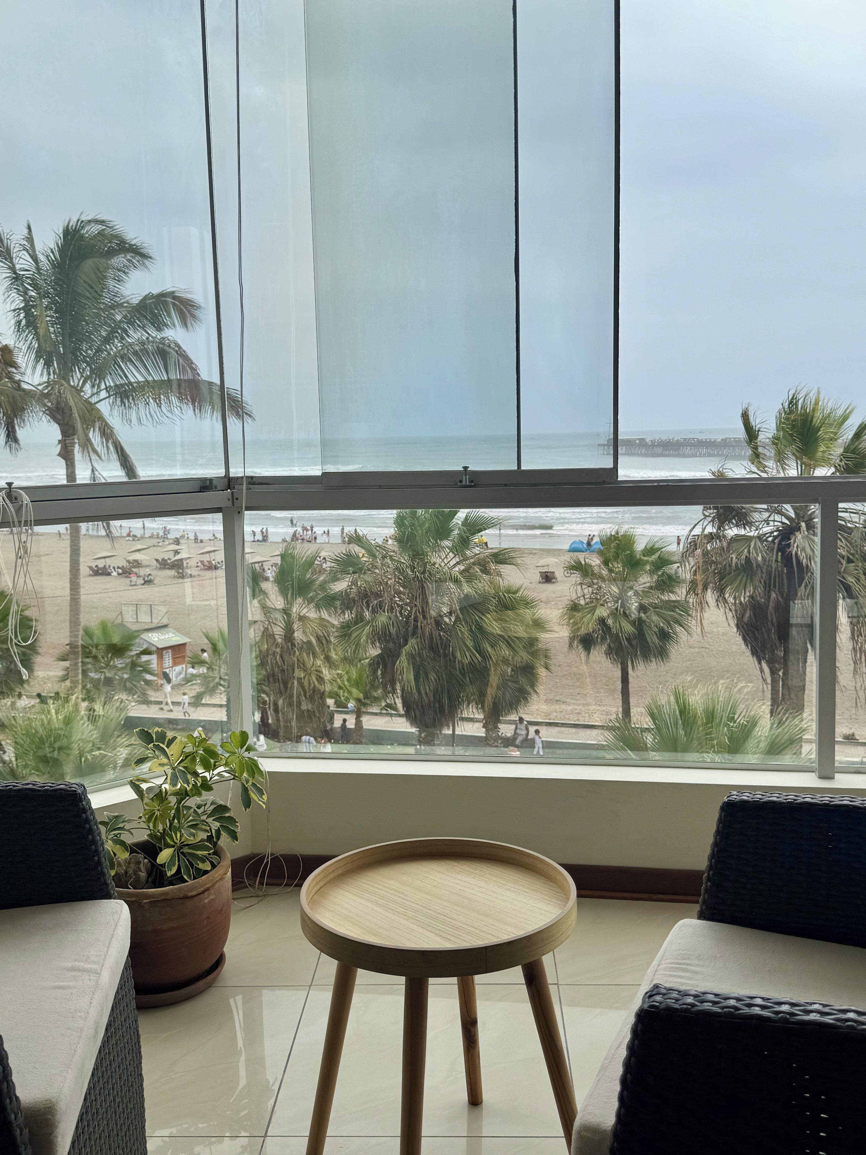 Ein Balkon mit Blick auf den Strand, ein runder Holztisch und zwei Korbsüpfchen.