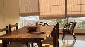 A dining area with a wooden table and chairs, large windows with curtains, and a view of the beach.