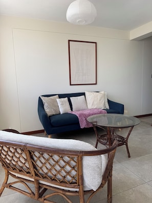 Una sala de estar con un sofá azul, una mesa de centro de vidrio y una silla de mimbre.