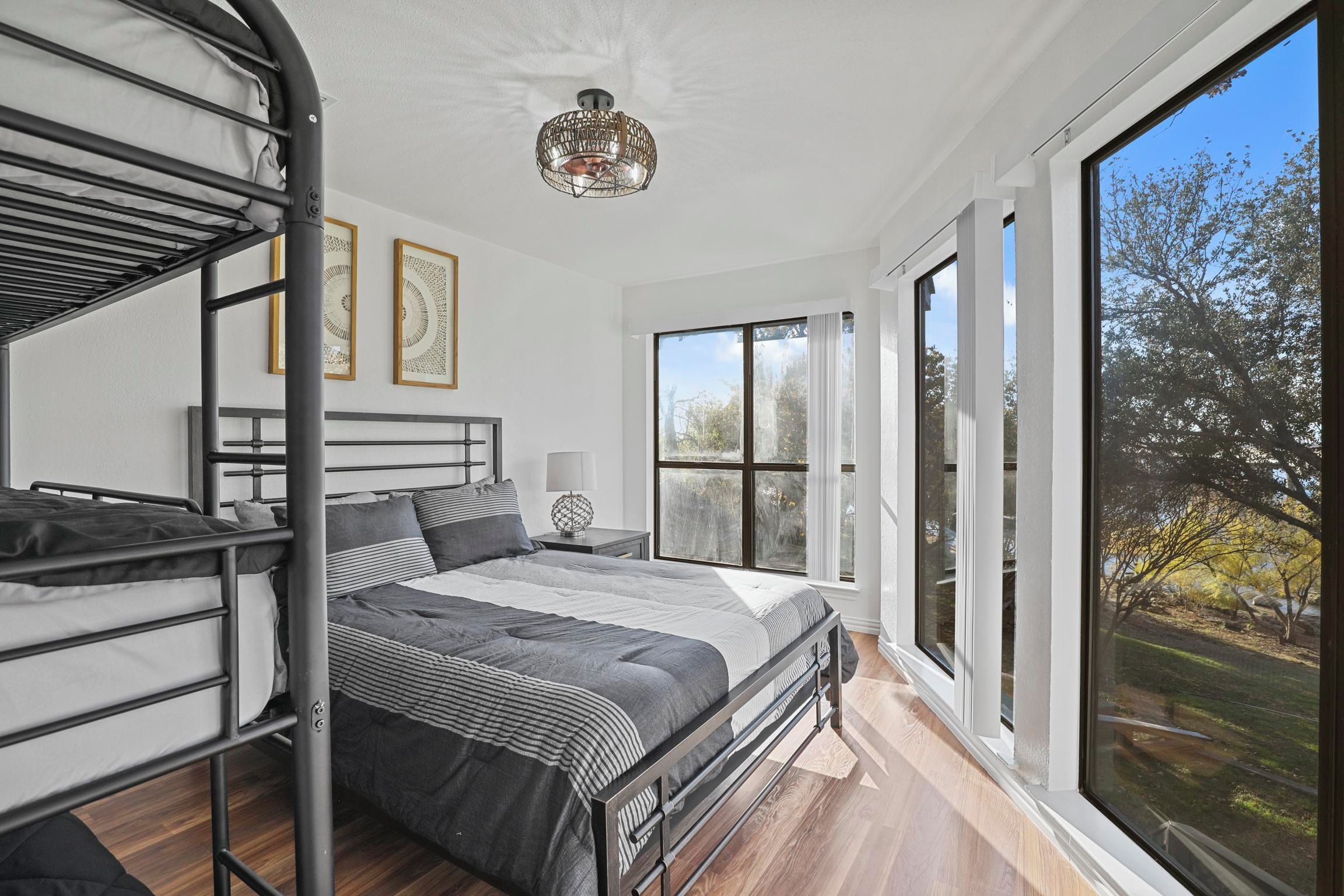 A bedroom with bunk beds, a bedside table with a lamp, and a large window offering a view of trees.