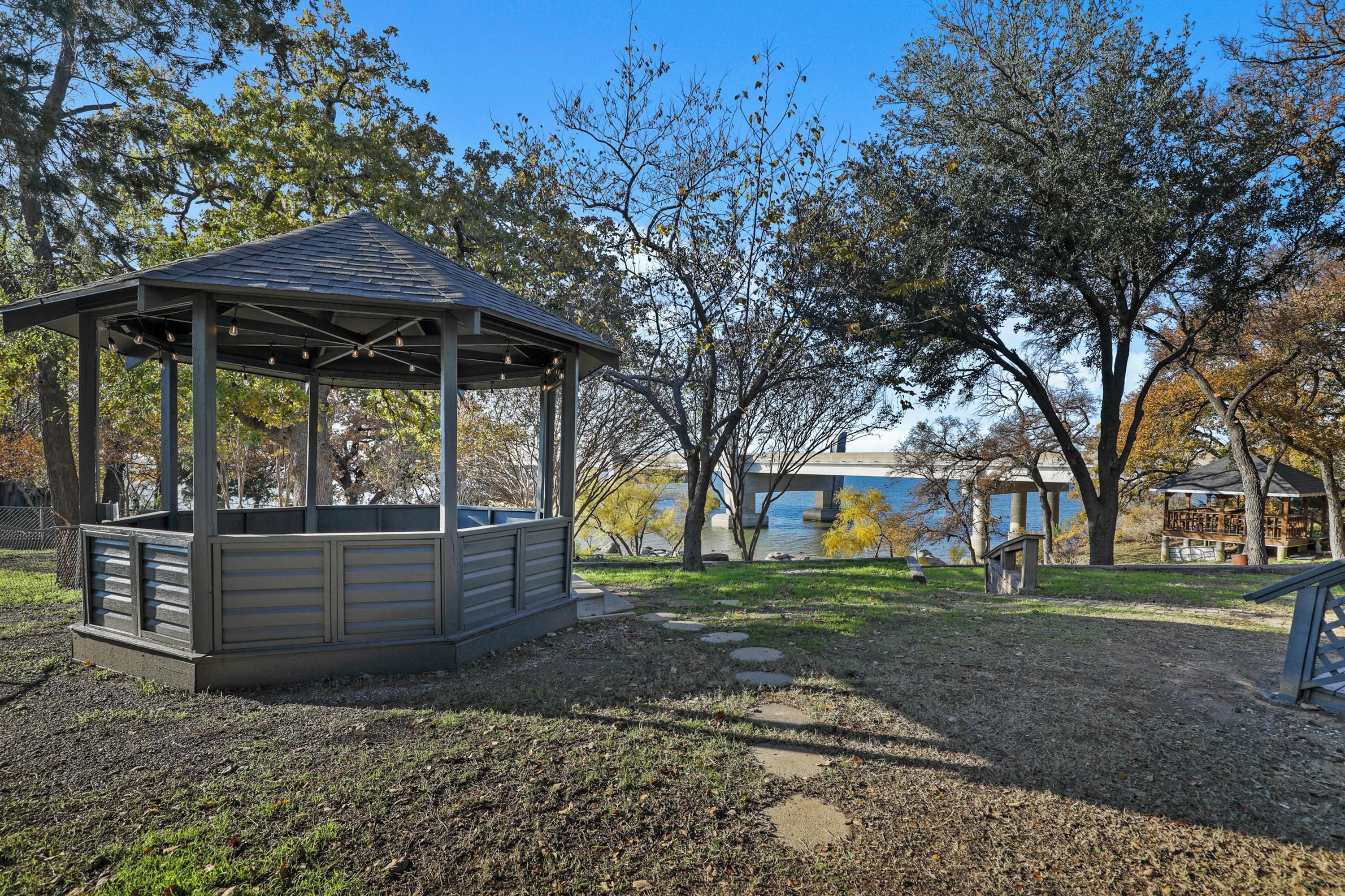 A gazebo with a sloped roof and a wooden structure, surrounded by trees and a body of water.