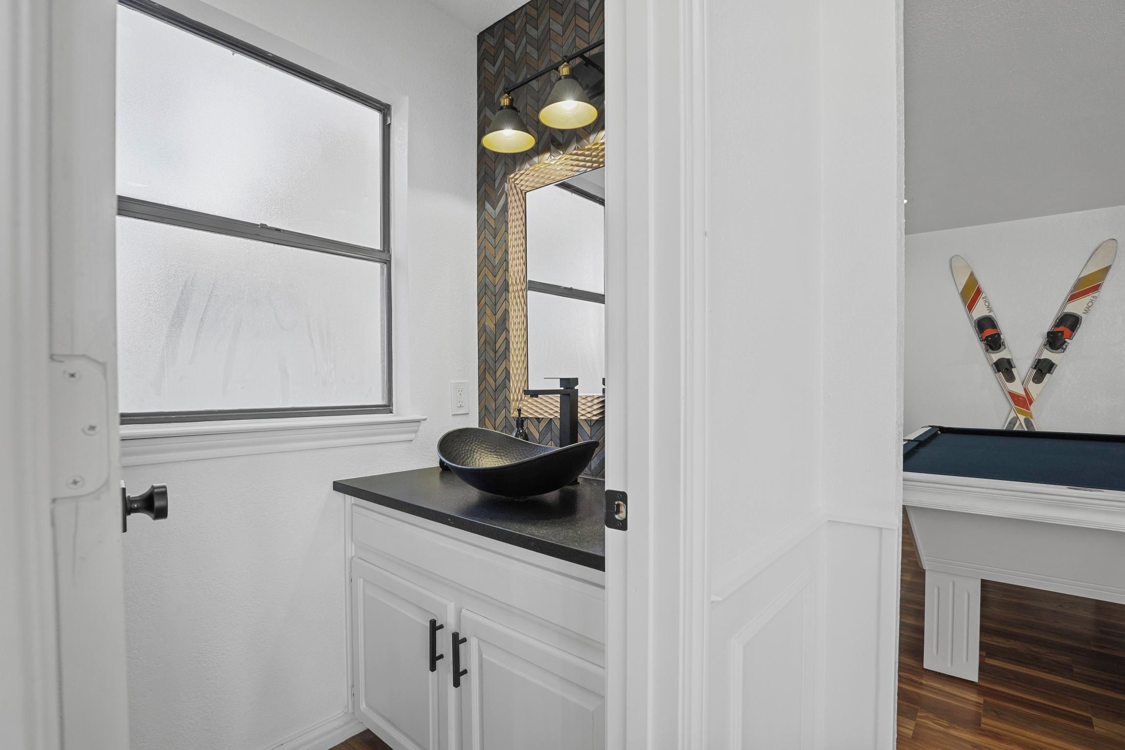 A bathroom with a white vanity, a black bowl sink, and a mirror with a herringbone-patterned backsplash.