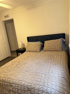 A bedroom with a large bed, two pillows, a bedside table with a lamp, and a door leading to another room.