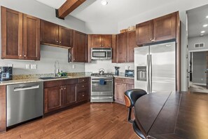 A modern kitchen with wooden cabinets, stainless steel appliances, and a granite countertop. - Newpark Terrace Retreat - Private Hot Tub + Nature Views • Walk to Shuttle (Park City)