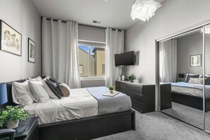Ein modernes Schlafzimmer mit Bett, Nachttisch, Fernseher und einem großen Spiegel.