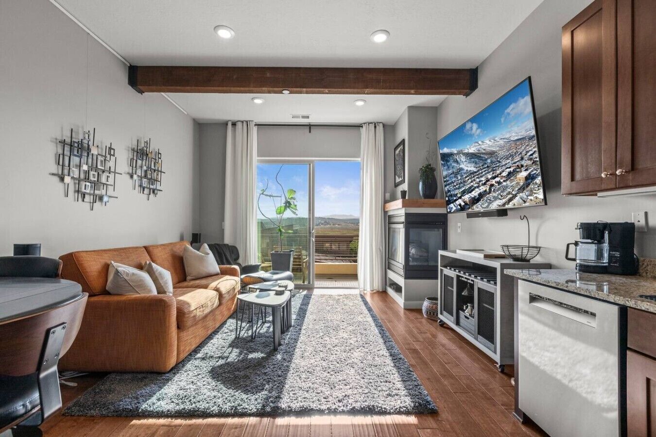 Uma sala de estar moderna com sofá, mesa de centro e vista para uma varanda externa através de uma porta de vidro.