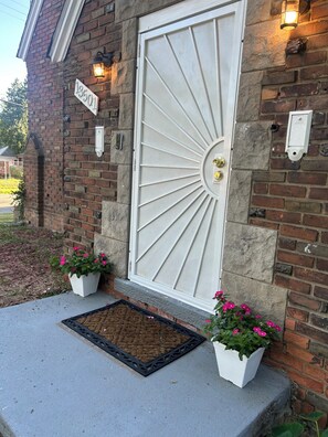 A house with a white door, a brick exterior, and two flower pots on the porch. - Spacious 6-bedroom house with AC in vibrant Detroit (Detroit)