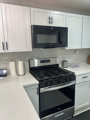 A modern kitchen with white cabinets, a stainless steel stove, and a black microwave. - Spacious 6-bedroom house with AC in vibrant Detroit (Detroit)