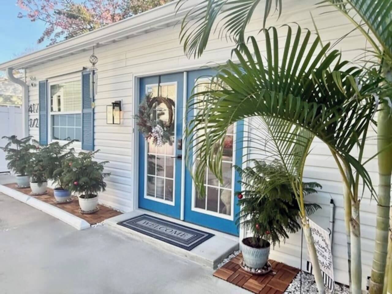 Une maison avec une porte bleue, un paillasson et des plantes en pot.