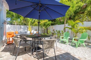 An outdoor patio with a round table, chairs, and a large umbrella. - Dunedin's Finest St - Walk Downtown & Waterfront - Palms Cottage (Dunedin)