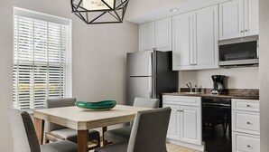 Una cocina con armarios blancos, un refrigerador de acero inoxidable, un lavavajillas y una mesa de comedor con sillas.