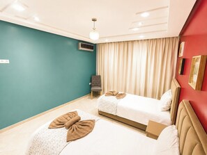 Ein Hotelzimmer mit zwei Betten, einem grauen Sessel, einer Deckenleuchte und einer Wand-Klimaanlage.