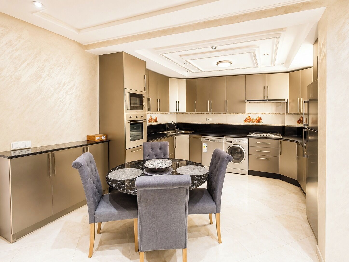 A modern kitchen with a dining area, featuring a round table with chairs, built-in appliances, and a light-colored tiled floor.