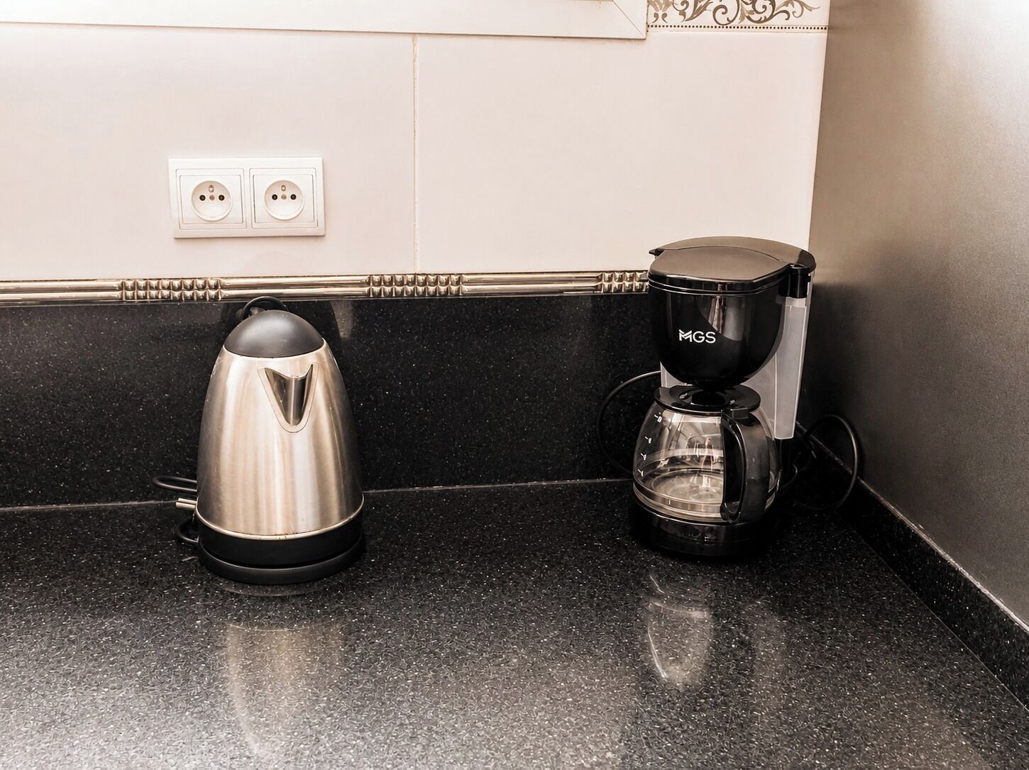 Una encimera de cocina con un hervidor de acero inoxidable y una cafetera negra.