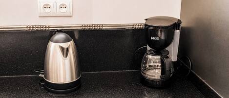 Una encimera de cocina con un hervidor de acero inoxidable y una cafetera negra.