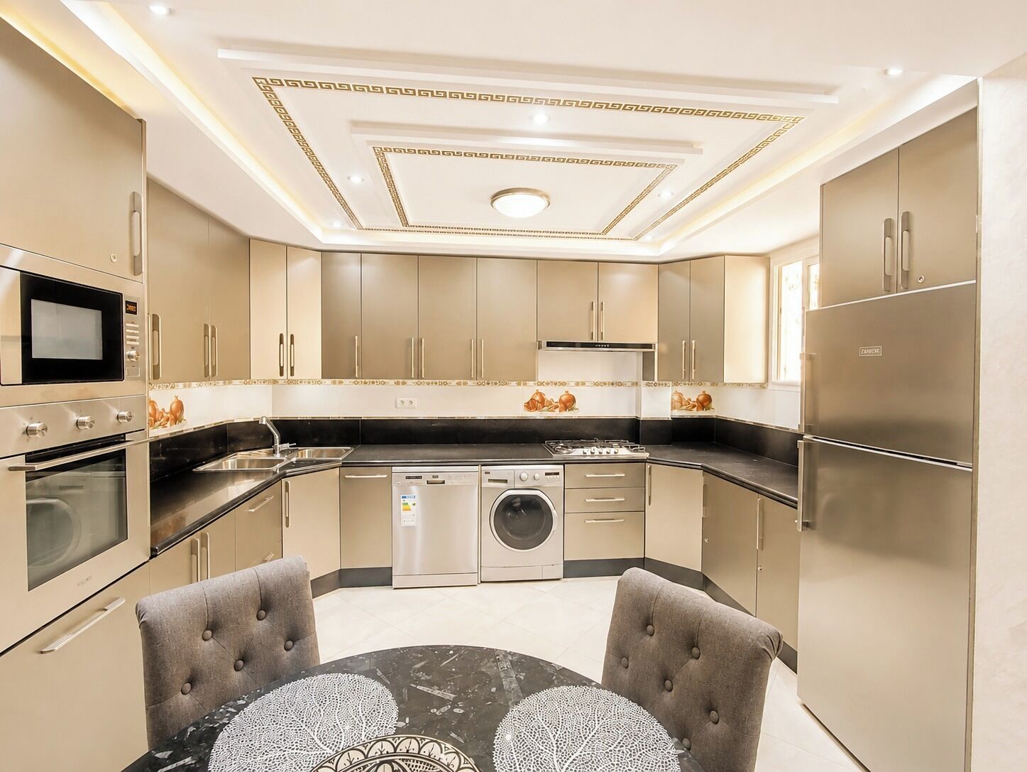 A modern kitchen with built-in appliances, a dining area with a marble table, and a decorative ceiling.