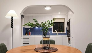 A modern kitchen with white cabinets, a blue backsplash, and a dining area with a round table and chairs. - KozyGuru | Broadmeadows | Cozy Home Near Airport (Broadmeadows)