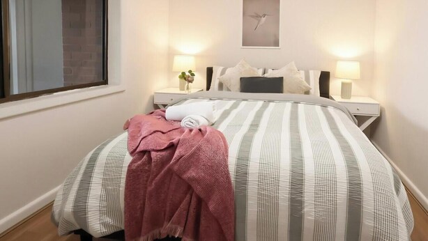 Ett hotellrum med en säng, två sängbord, ett fönster och en tavla som hänger på väggen.
