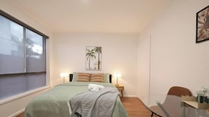 Une chambre d’hôtel avec un lit, deux lampes de chevet, une petite table, une chaise et une fenêtre.