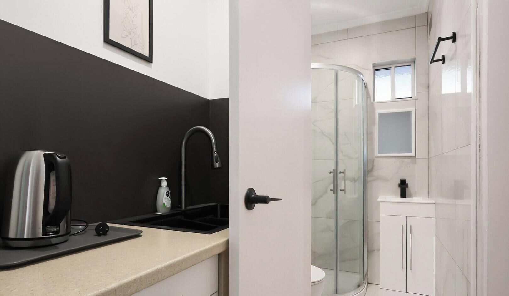 A modern bathroom with a glass shower enclosure, a sink with a faucet, and a kettle on the countertop.