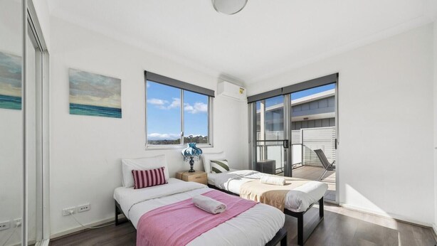 A modern bedroom with two beds, a large window, and a balcony. - KozyGuru | Wentworthville | Luxury Penthouse (Wentworthville)