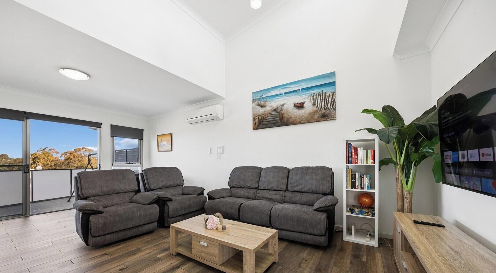 A modern living room with a grey sofa set, a wooden coffee table, and a bookshelf.