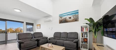 A modern living room with a grey sofa set, a wooden coffee table, and a bookshelf.