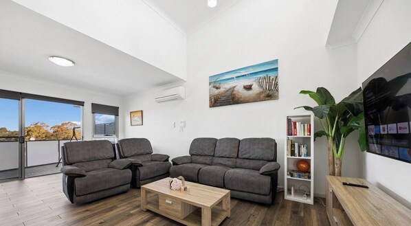A modern living room with a grey sofa set, a wooden coffee table, and a bookshelf.