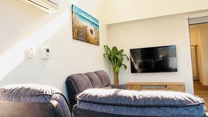 A living room with a sofa, a flat-screen TV, and a painting on the wall. - KozyGuru | Wentworthville | Luxury Penthouse (Wentworthville)