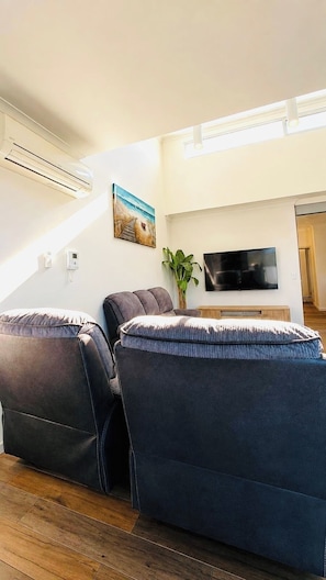 A living room with a sofa, a flat-screen TV, and a painting on the wall. - KozyGuru | Wentworthville | Luxury Penthouse (Wentworthville)