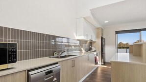 A modern kitchen with a microwave, dishwasher, and stainless steel appliances. - KozyGuru | Wentworthville | Luxury Penthouse (Wentworthville)