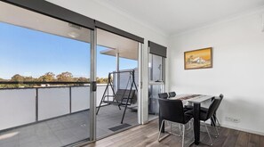 A balcony with a dining table and chairs, a swing, and a glass door leading to an outdoor area.