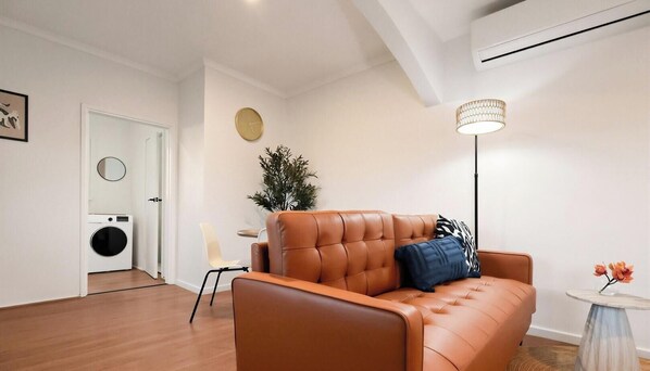 Ein modernes Wohnzimmer mit Ledersofa, einer runden Wanduhr, einem Blumentopf und einer Stehlampe.