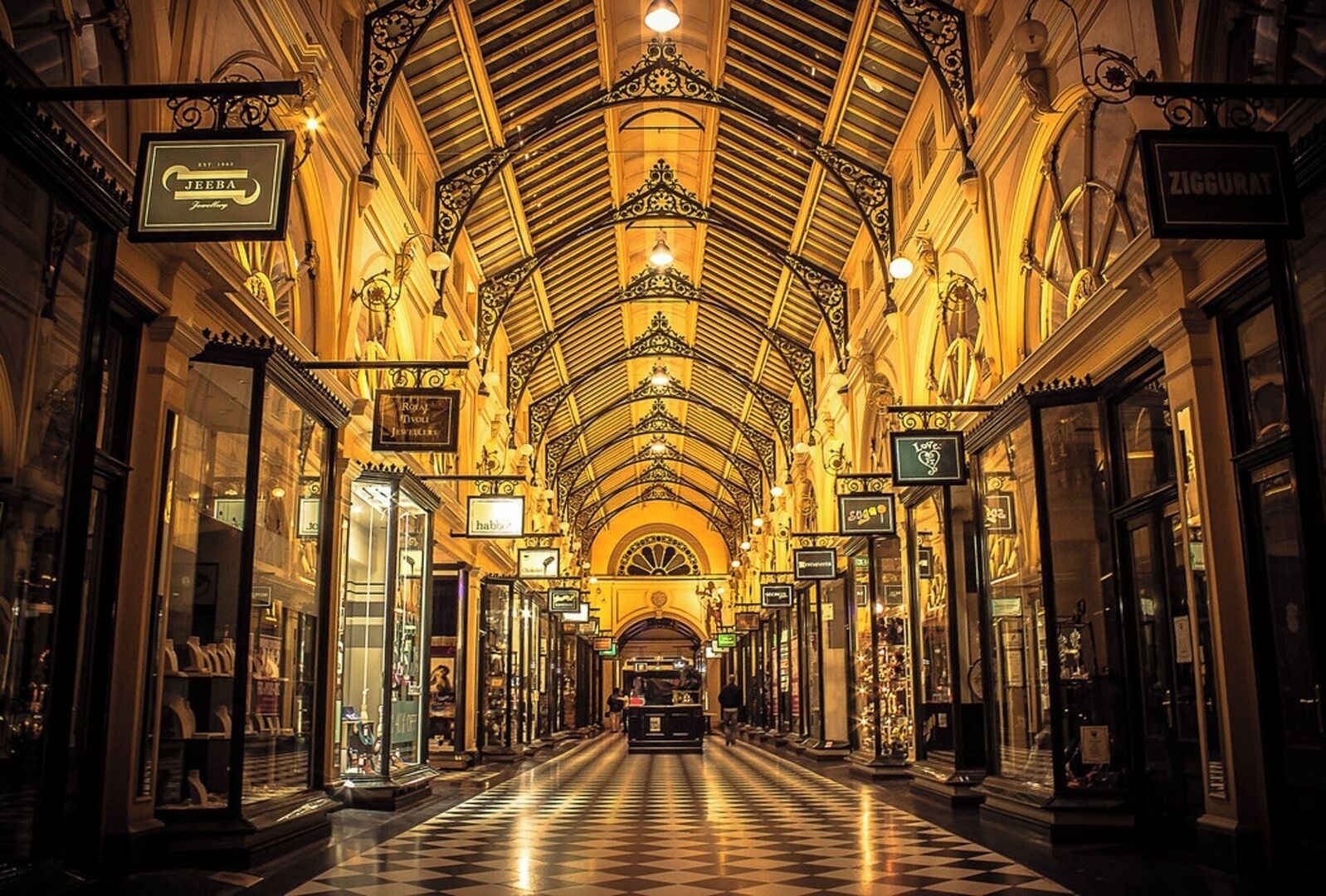 An ornate indoor shopping arcade with a checkered floor and hanging signs for various shops.