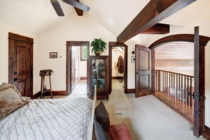 Een slaapkamer met een groot bed, een houten plafondventilator en uitzicht op de omgeving via een geopende deur.