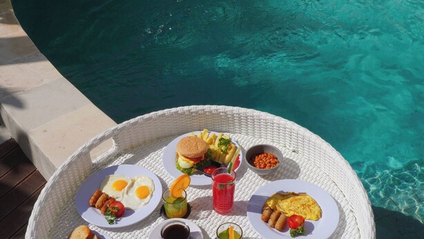 A round table with a variety of food items and drinks, placed by a poolside. - Private 2BR Villa & Pool - Rice Field Views - Canggu (Dalung)