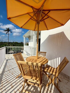 A wooden table and chairs under a large umbrella on a balcony with a white railing, overlooking a view of a building and palm trees. - Private 2BR Villa & Pool - Rice Field Views - Canggu (Dalung)