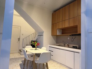 A modern kitchen with white cabinetry, a dining table with chairs, and a staircase leading to another level. - Private 2BR Villa & Pool - Rice Field Views - Canggu (Dalung)