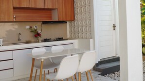 A modern kitchen with wooden cabinets, a white countertop, and a dining area with white chairs. - Private 2BR Villa & Pool - Rice Field Views - Canggu (Dalung)