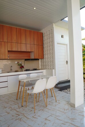 A modern kitchen with wooden cabinets, a white countertop, and a dining area with white chairs. - Private 2BR Villa & Pool - Rice Field Views - Canggu (Dalung)