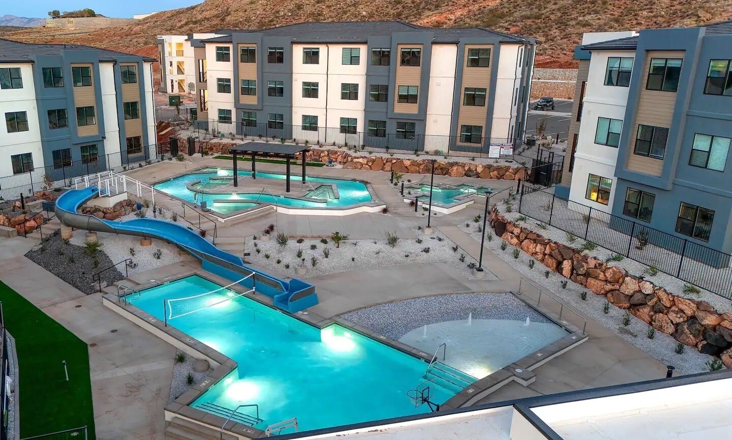 A modern hotel with multiple swimming pools, including a large central pool and a smaller pool with a slide.