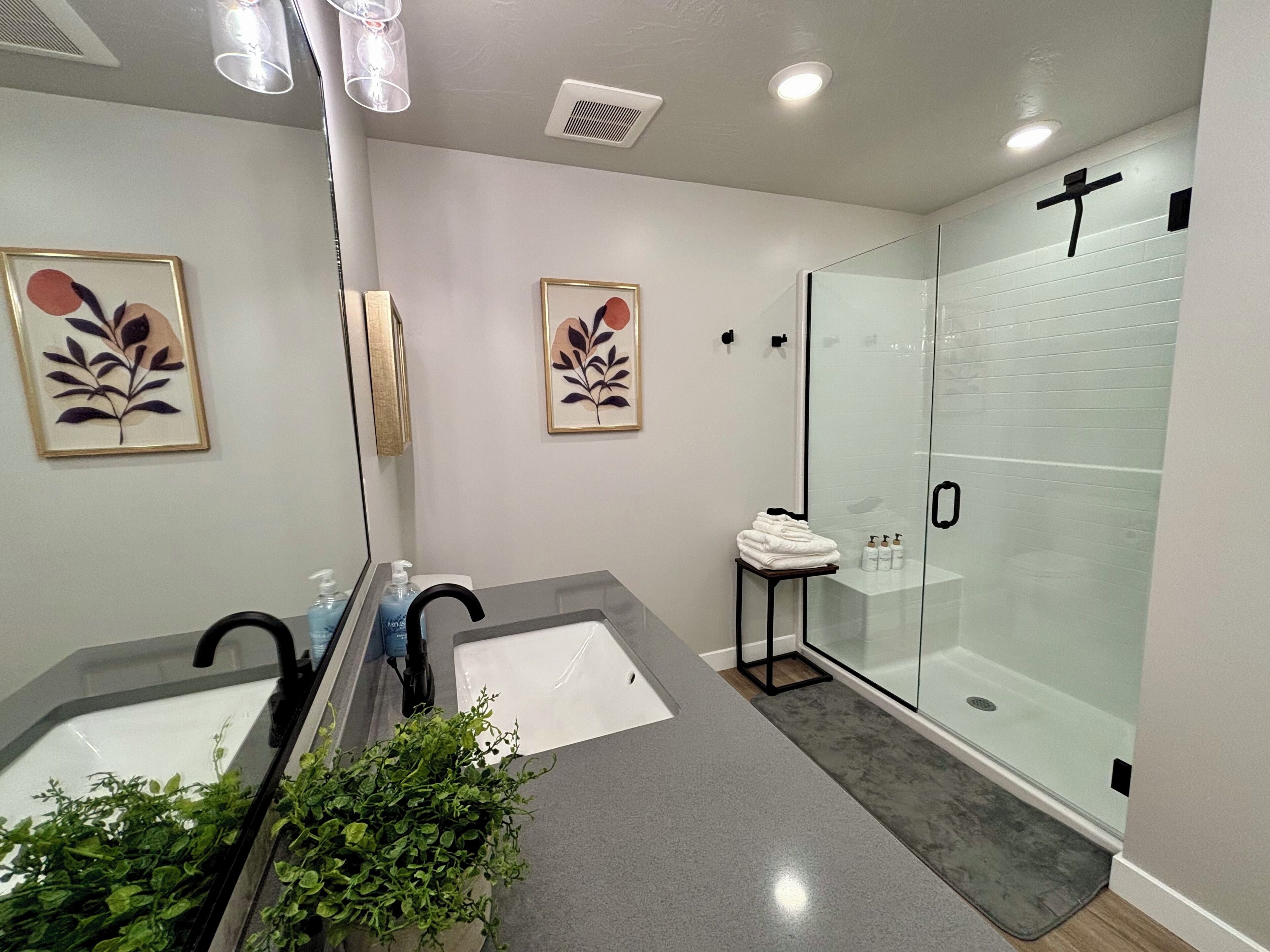 Ein modernes Badezimmer mit Duschkabine aus Glas, einem Waschbecken inklusive Spiegel und zwei gerahmten Kunstwerken an der Wand.